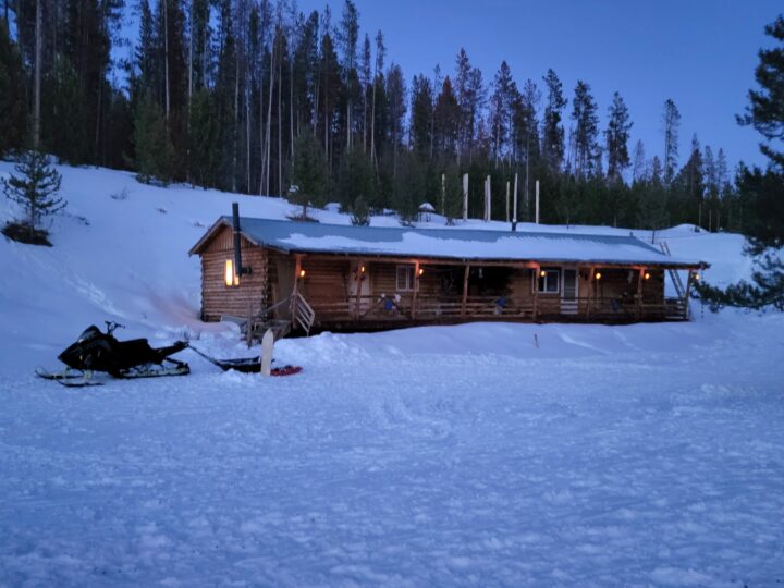 A snow-covered cabin with a snowmobile parked nearby, providing the ideal winter lodging experience.