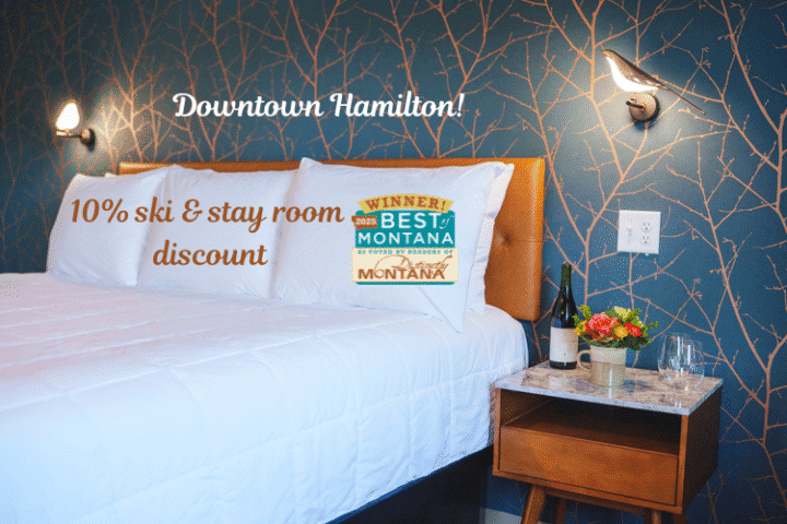 A neatly made bed at City Center Motel in downtown Hamilton, with text promoting a 10% ski and stay discount and a "Best of Montana" winner badge.