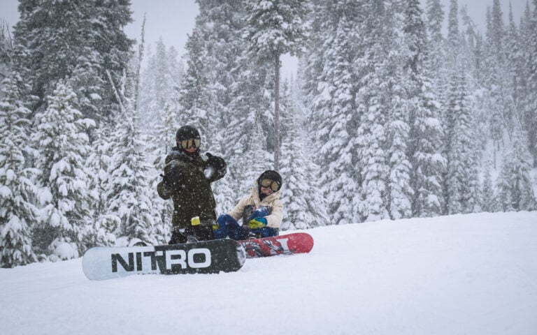 Two people enjoying the snow-covered slope at Lost Trail Ski Area with their snowboards.