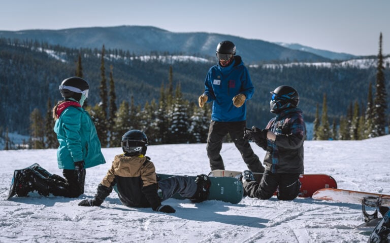 A group of people sitting on the snow at Lost Trail Ski Area with snowboards.