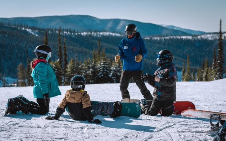 A group of people sitting at Lost Trail Ski Area with snowboards.