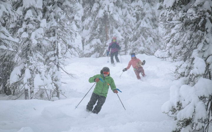 A group of people snowboarding down a snowy trail at Lost Trail Ski Area.