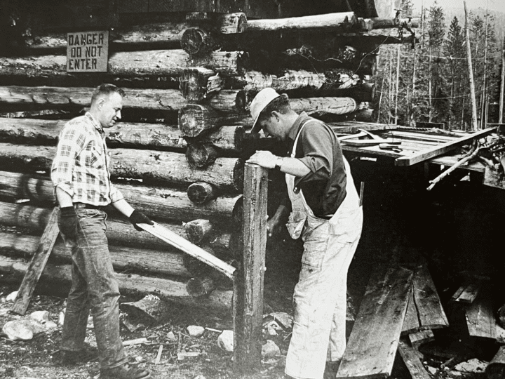 an old photo of Two men standing next to a log building at Lost Trail Ski Area.