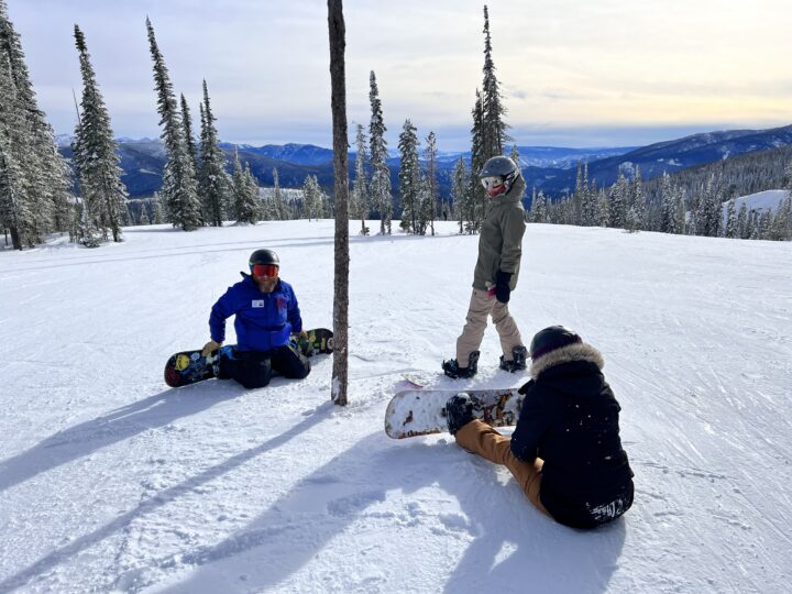 Three people sitting on the ground with snowboards at Lost Trail.