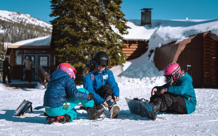 A group of people sitting in the snow with snowboards at Lost Trail ski area.