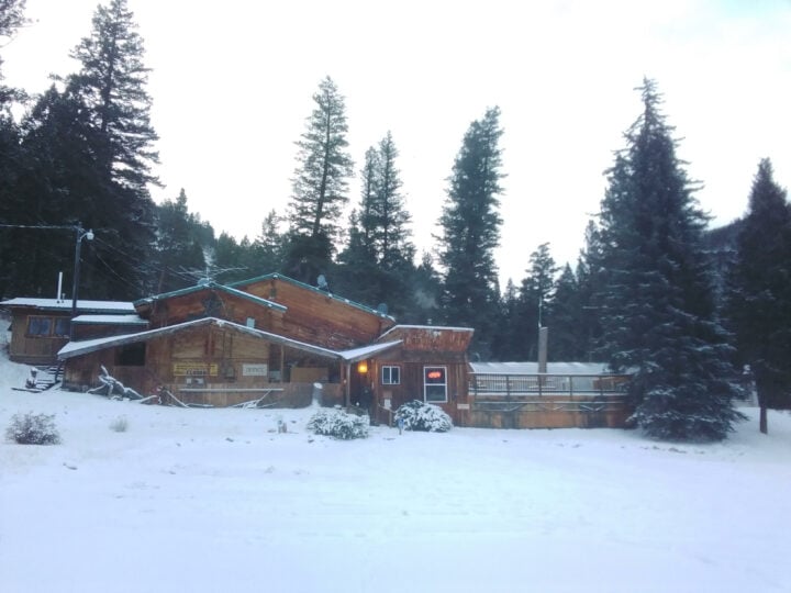 A cozy cabin nestled in the snow-covered wilderness, surrounded by majestic trees.