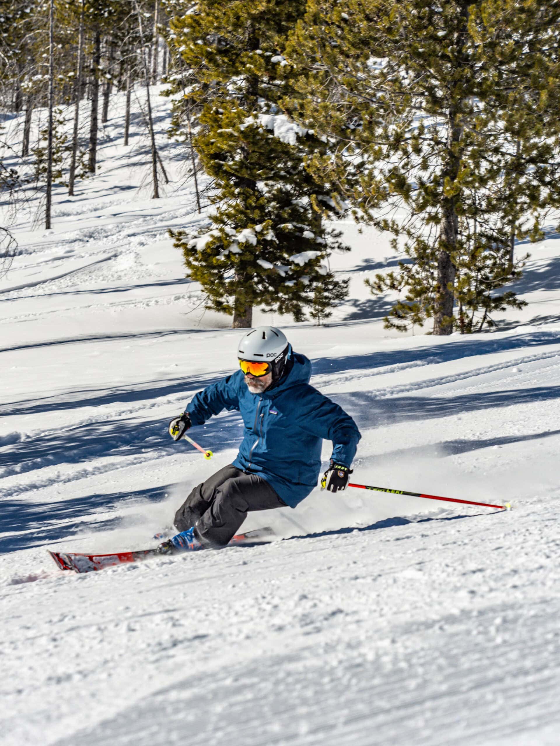 Skier in a blue jacket and helmet descends a snowy slope at Lost Trail, with trees in the background on a sunny day, reminiscent of Deb Armstrong's elegant ski style.