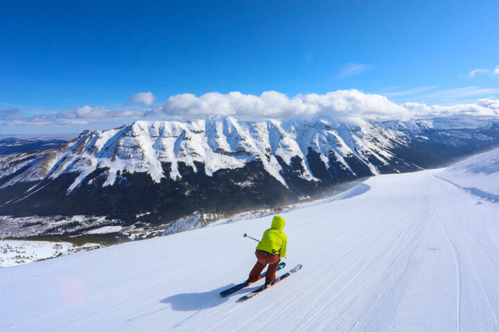 A person skiing down a snow covered slope with mountains in the background at Lost Trail Ski Area.
