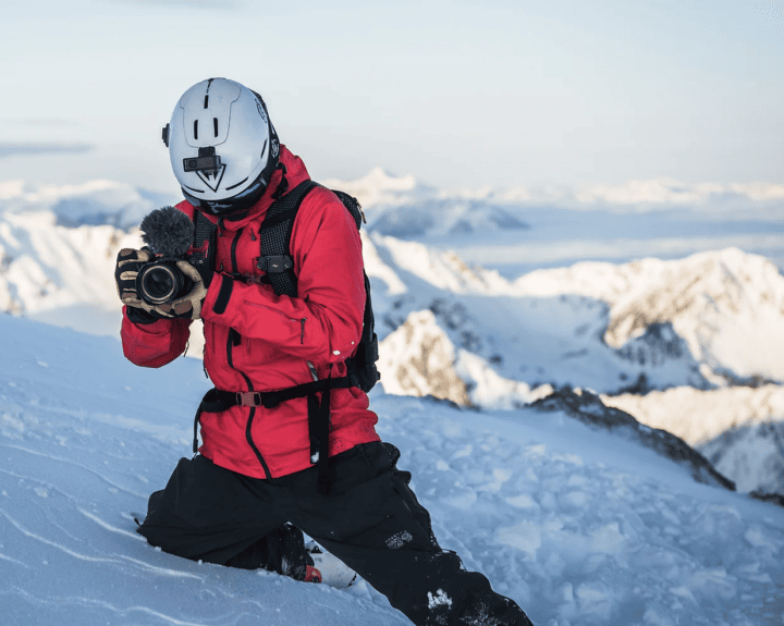 A man capturing stunning footage with a camera on top of a snowy mountain.